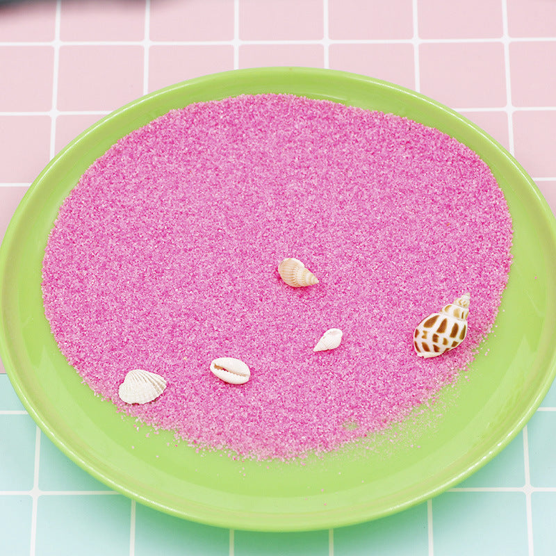 Pink sand with shells on a green plate against a pink and green tiled background