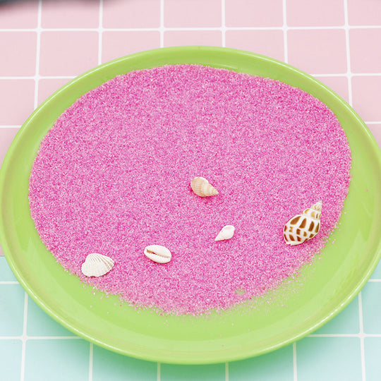 Pink sand with shells on a green plate against a pink and green tiled background