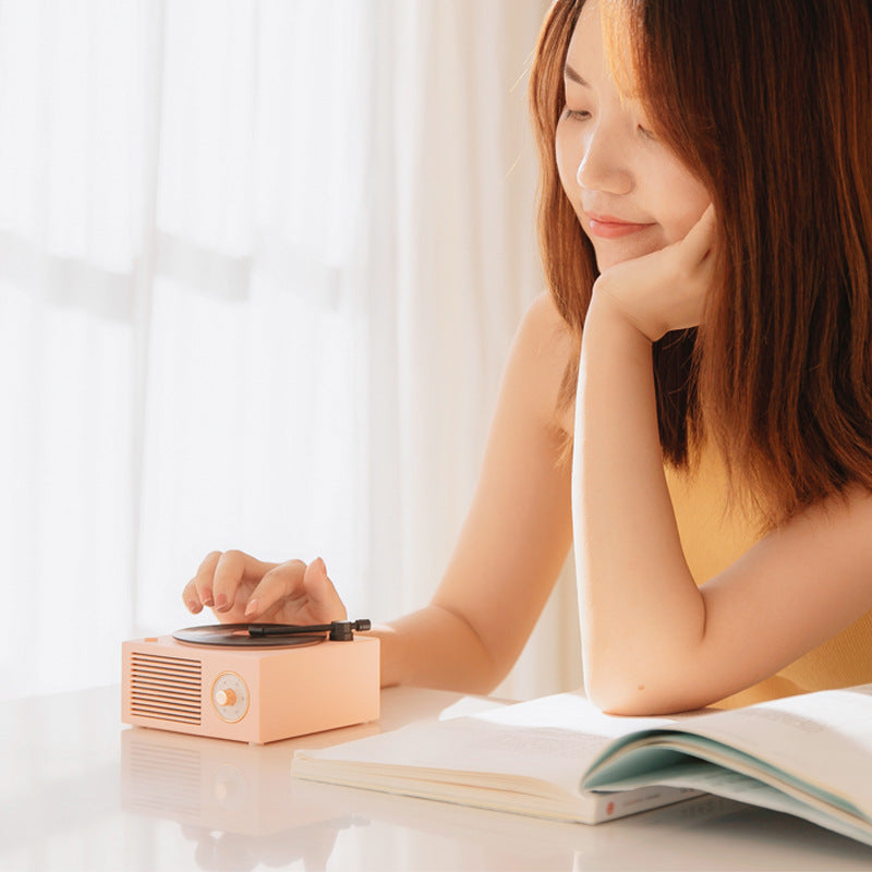 Woman sitting at a table with a record player and open book, smiling.
