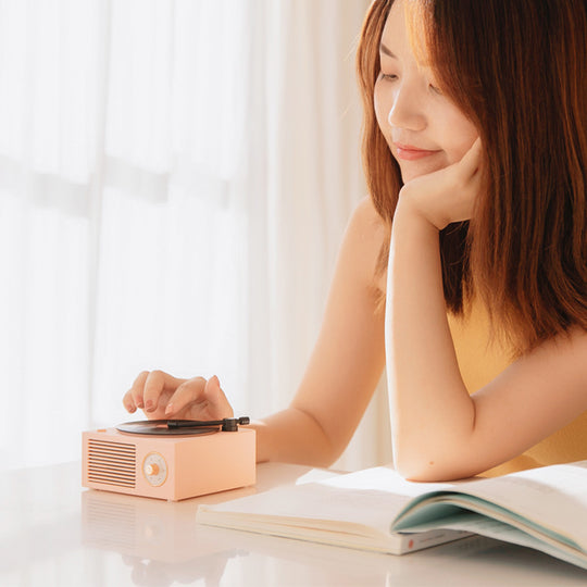 Woman sitting at a table with a record player and open book, smiling.