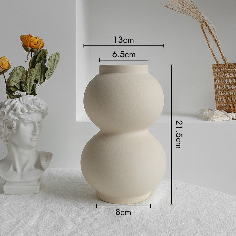 Beige ceramic vase with measurements on a white surface with decorative items.