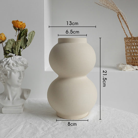 Beige ceramic vase with measurements on a white surface with decorative items.