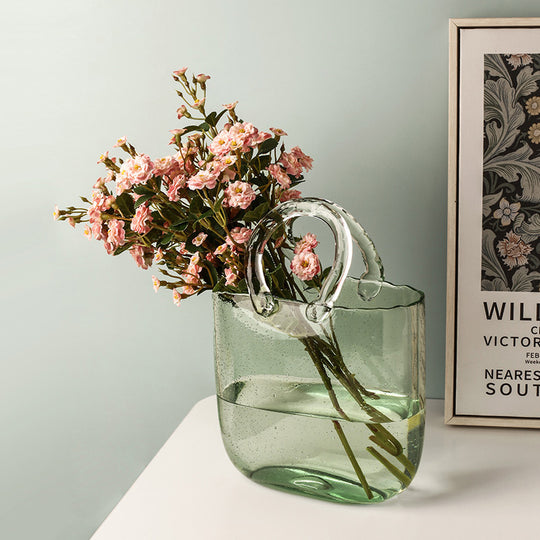 Green glass vase with floral arrangement on a light surface against a light gray wall.