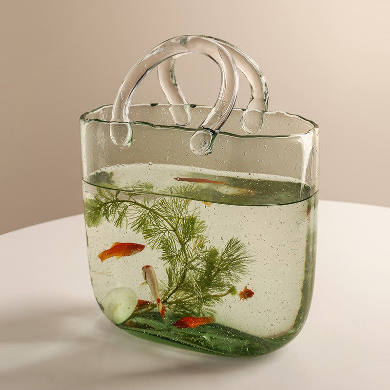 Clear handbag filled with water, plants, and small fish on a light background