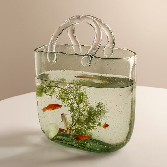 Clear handbag filled with water, plants, and small fish on a light background