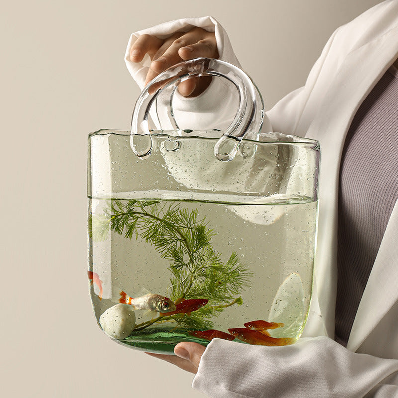 Clear handbag with water and small plants and fish, held by a person wearing a white shirt.