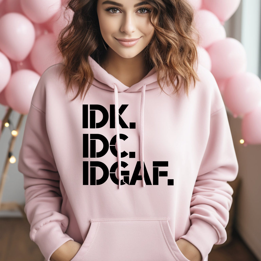 Person wearing a pink hoodie with 'IDK, IDC, IDGAF' text in a room with pink balloons.