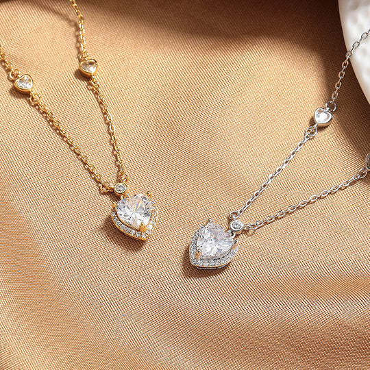 Two heart-shaped diamond pendants on gold and silver chains on a beige fabric background.