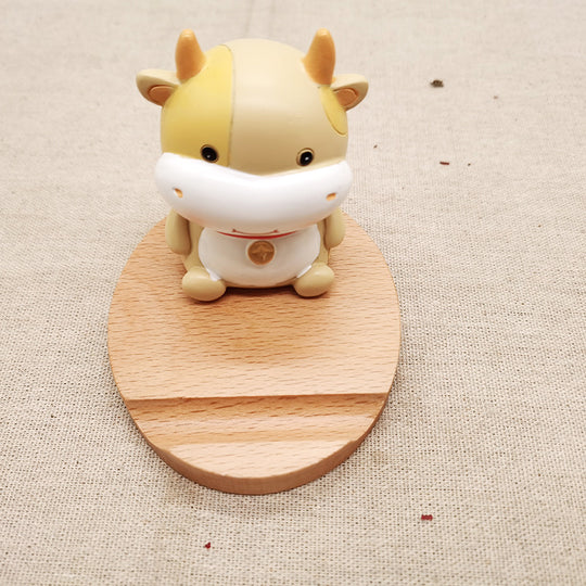 Cute cow-shaped figurine on a wooden stand against a beige fabric background