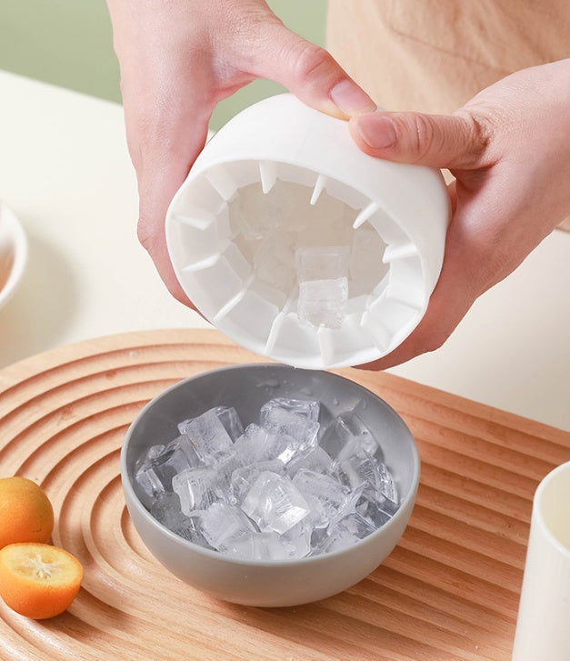 Person using a silicone ice cube tray to fill a bowl with ice cubes on a wooden surface.
