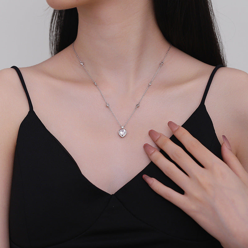 Woman wearing a delicate necklace with a heart pendant, touching her chest.