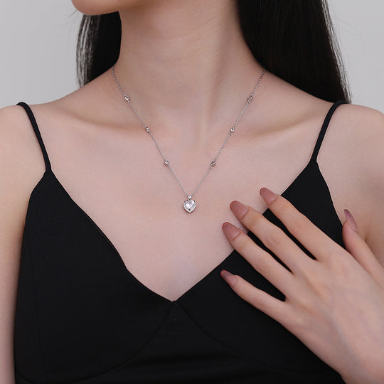 Woman wearing a delicate necklace with a heart pendant, touching her chest.