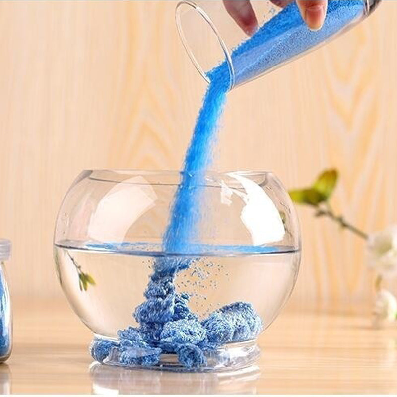 Blue powder being poured into a clear glass bowl on a wooden surface.