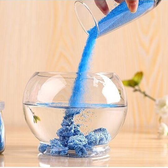 Blue powder being poured into a clear glass bowl on a wooden surface.