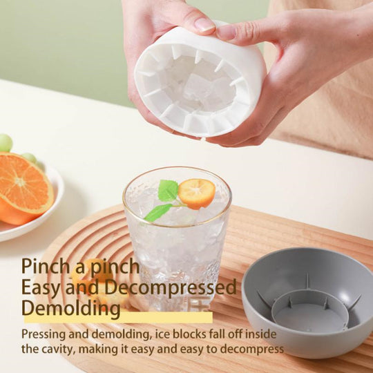 Ice cube tray being used to make ice cubes with a glass of water and fruit on a wooden surface.