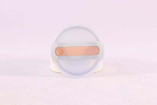 Clear container with a gold-colored object on a light purple background