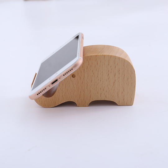 Wooden elephant phone stand holding a smartphone on a white background