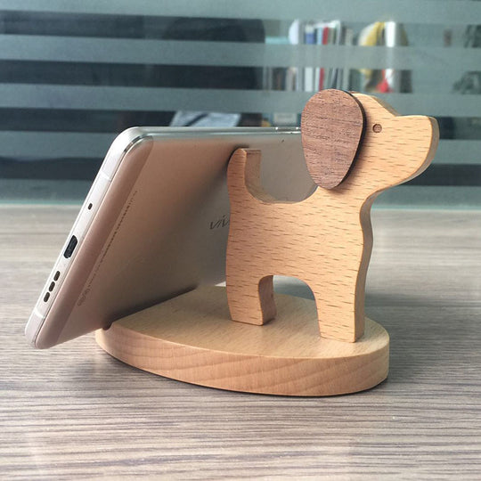 Wooden dog-shaped phone stand holding a smartphone on a wooden surface.