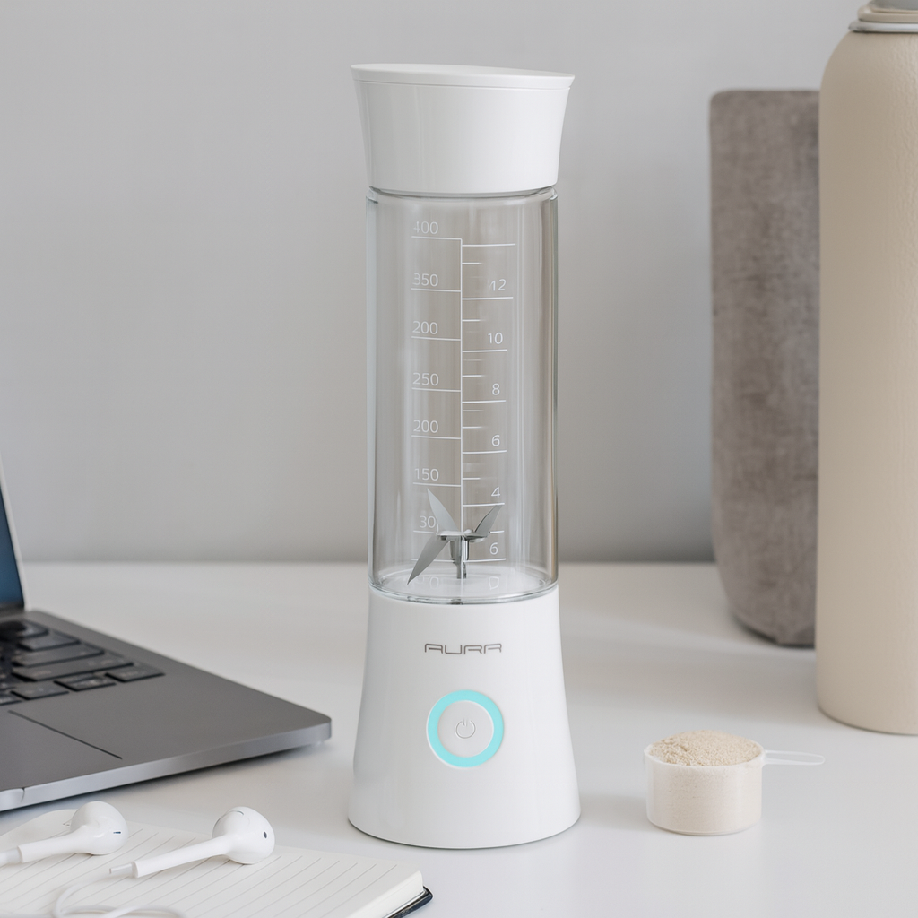 White and clear blender on a desk with a laptop and earphones in the background