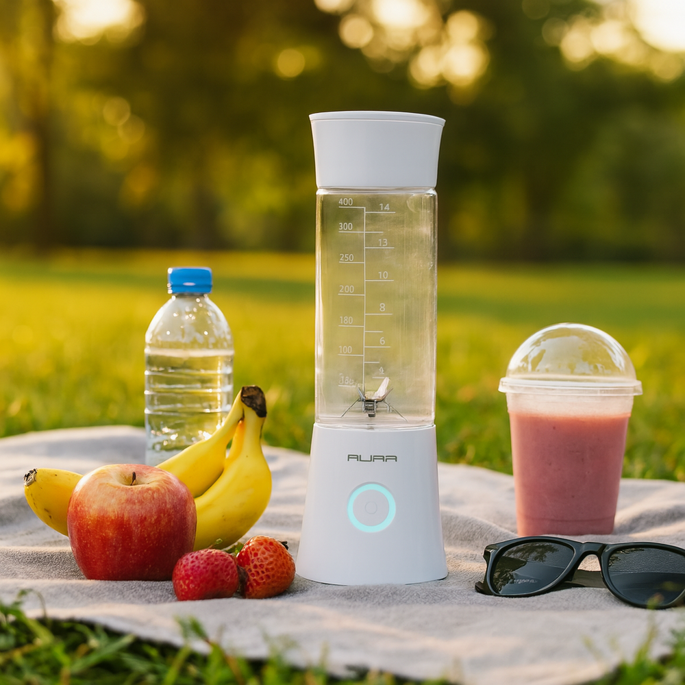Portable blender with fruits and a smoothie on a picnic blanket outdoors