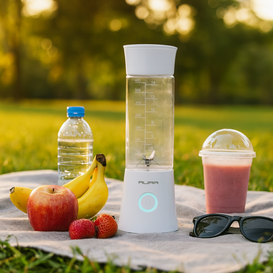 Portable blender with fruits and a smoothie on a picnic blanket outdoors