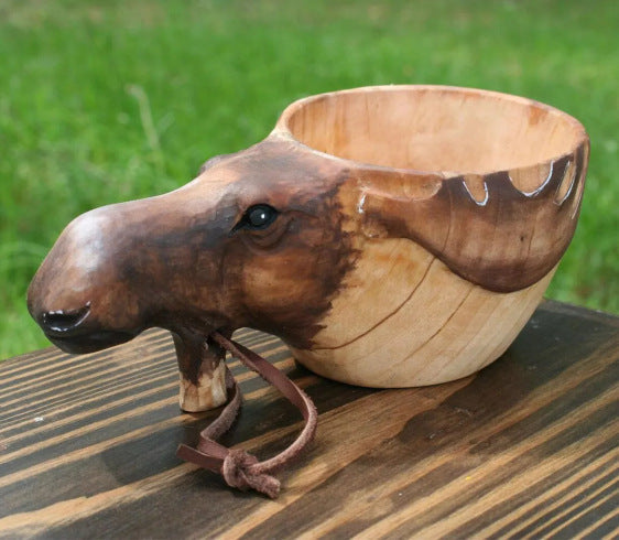 Wooden bowl shaped like a moose head on a wooden surface with grass in the background