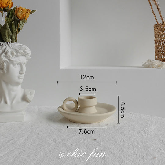 Small ceramic cup and saucer with dimensions on a textured surface, featuring a classical bust and flowers.