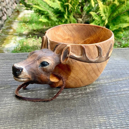Wooden bowl shaped like a deer head on a wooden surface with a natural background.