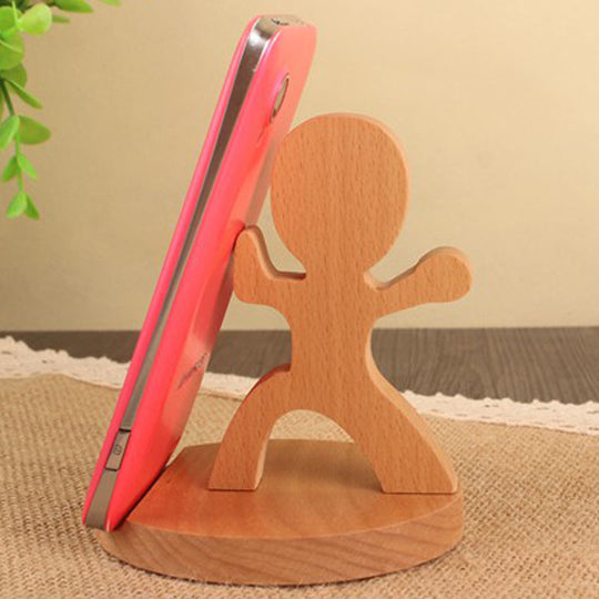 Wooden phone stand holding a pink phone on a textured surface with a plant in the corner.