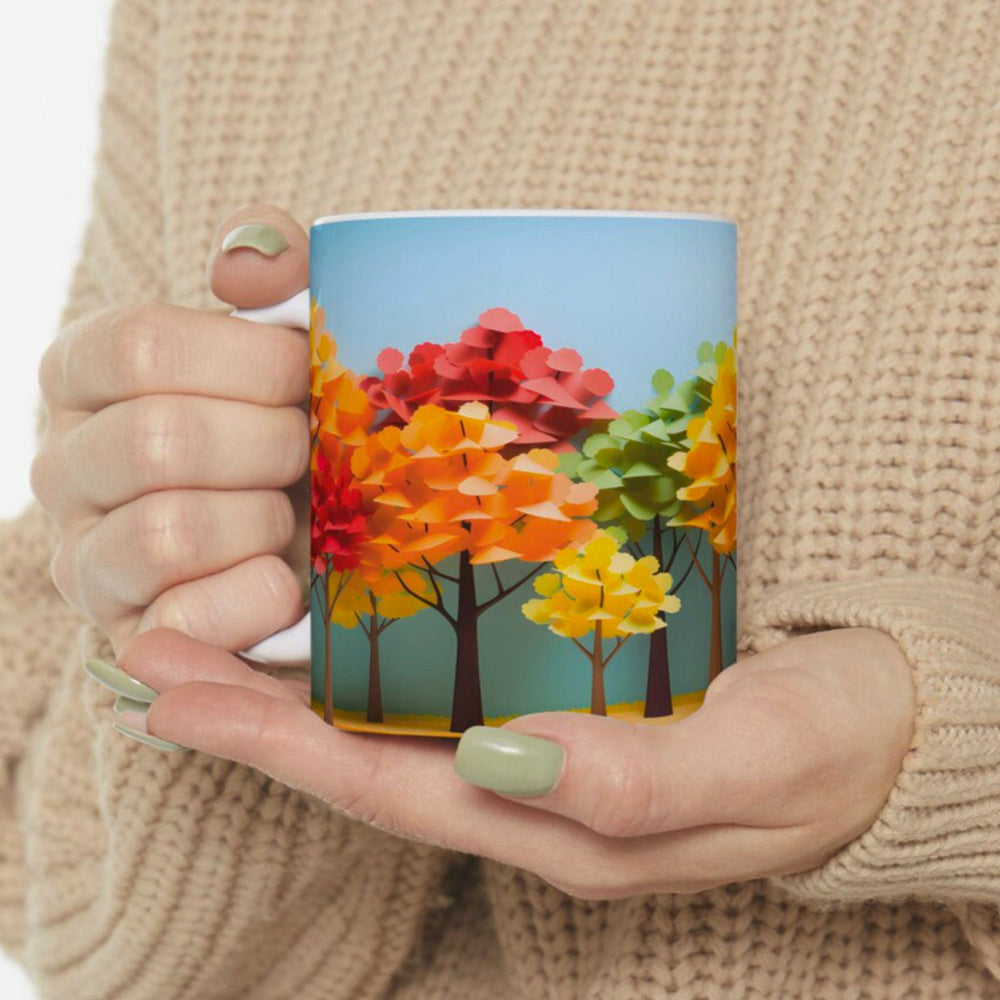 Person holding a mug with a colorful autumn tree design against a beige background