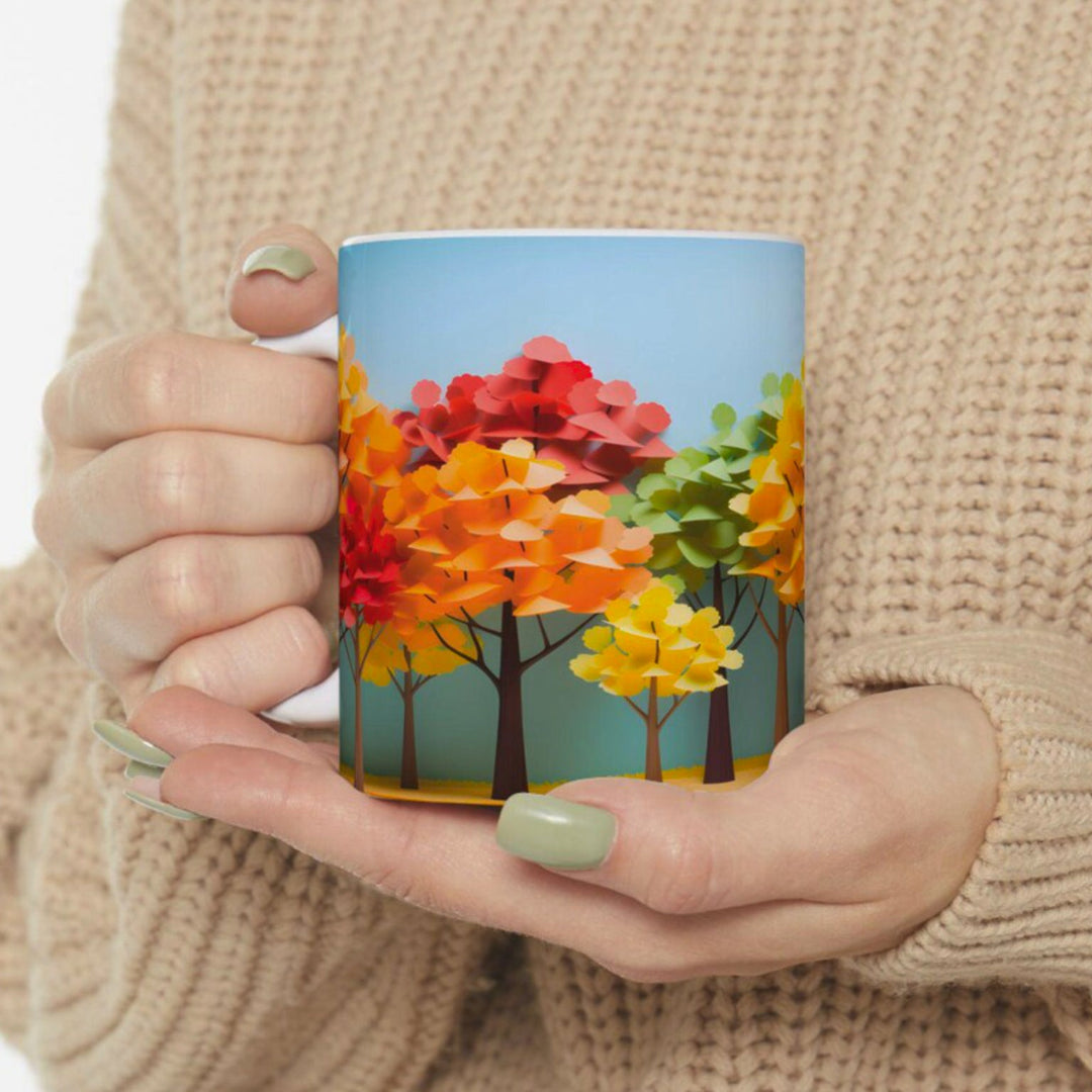 Person holding a mug with a colorful autumn tree design against a beige background