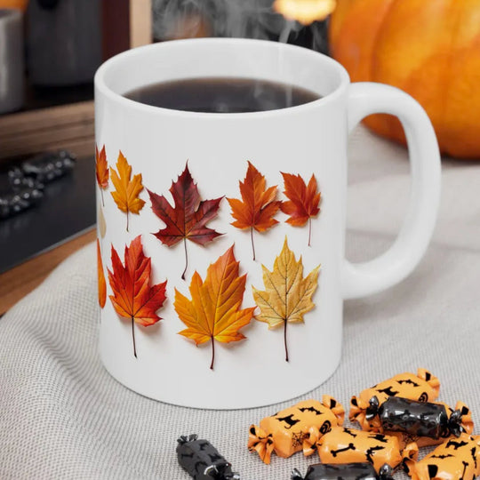 White mug with autumn leaf design on a table with pumpkins and cookies.