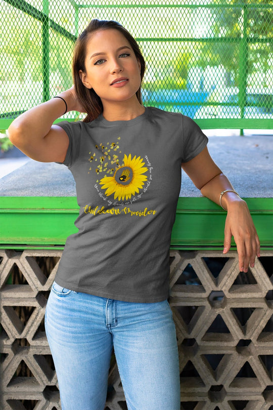 Woman wearing a gray t-shirt with a sunflower design and text, standing against a green metal fence.