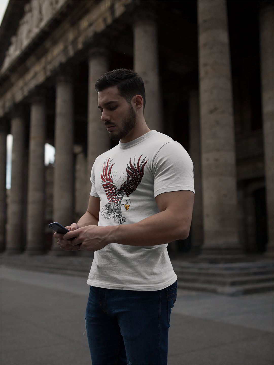 Man wearing a white t-shirt with an eagle design, standing in front of classical architecture.