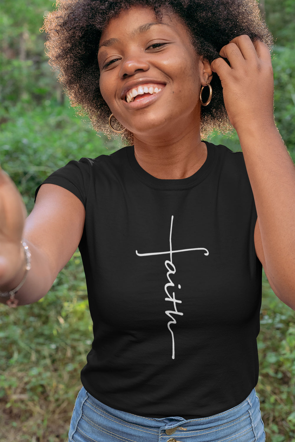 Woman wearing a black t-shirt with 'faith' printed on it, outdoors.