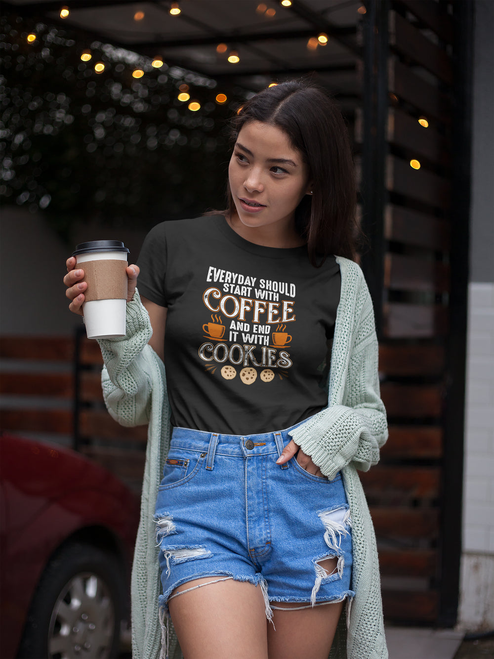 Woman wearing a black t-shirt with text and graphics, holding a coffee cup outdoors.